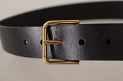 Bälte i svart kalvskinn med guldtonad metallspänne med logotyp.