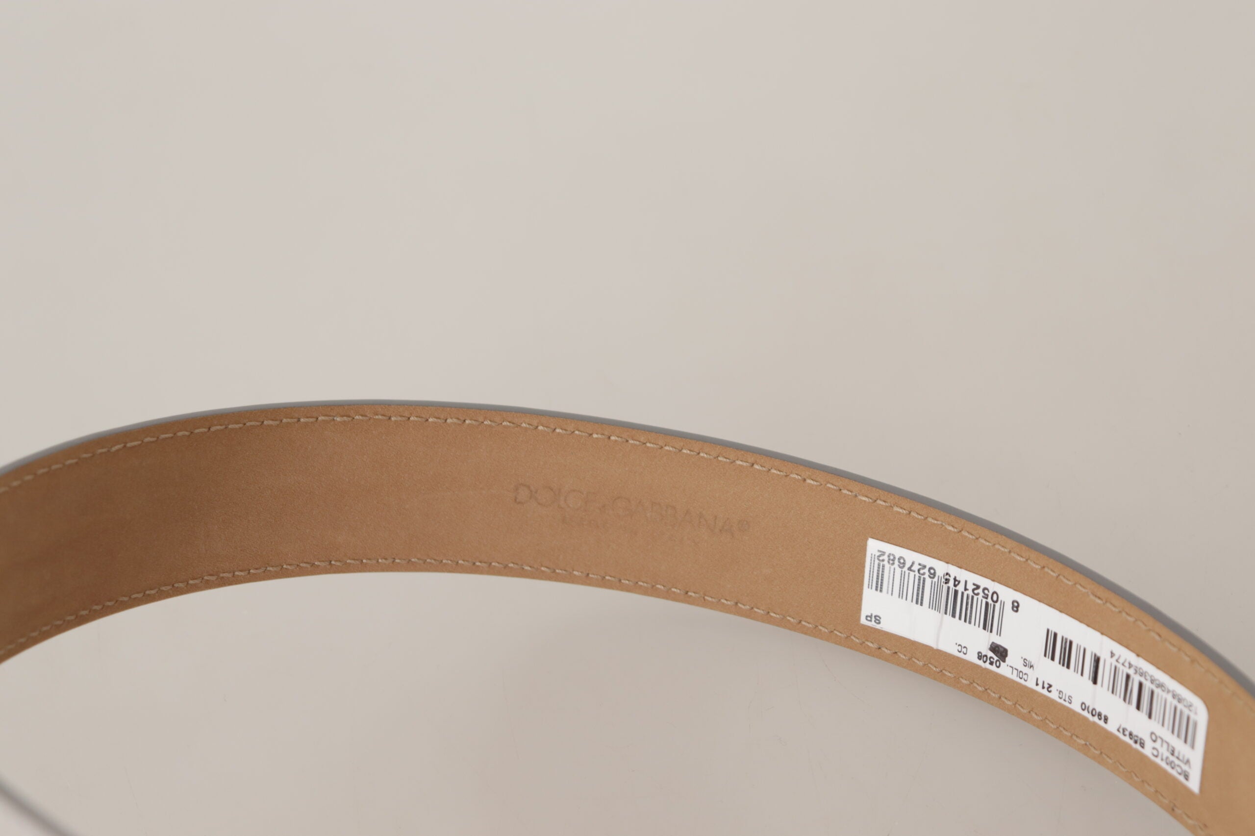 Silverfärgad läderbälte med guldtonad metallspänne och logo.